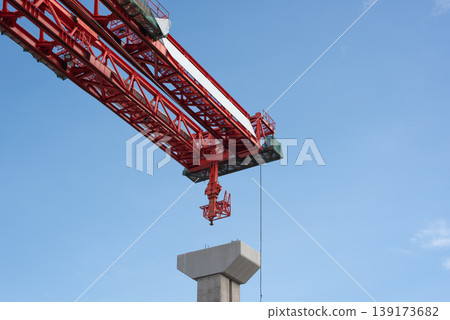 Close up red tower crane lifting concrete pillar against blue sky construction site heavy industry engineering structure and urban development concept 139173682