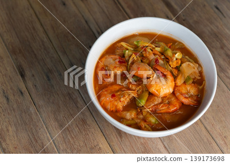 Close up Thai sour curry with shrimp and sesbania flowers in rich orange broth spicy and tangy flavor traditional cuisine served in bowl on wooden table 139173698
