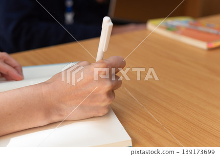 Close up hand writing in notebook with pen on wooden desk natural light workspace focus learning study note taking and productivity concept clean background 139173699