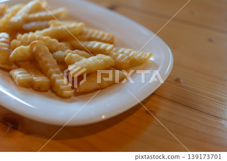Close up crispy french fries on white plate with golden texture and soft light on wooden table simple snack comfort food and casual dining concept 139173701