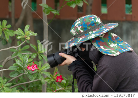 Photographer capturing red flowers with camera in garden wearing hat and protective clothing showing outdoor hobby nature exploration creativity and focus Photographer capturing red flowers with camera in garden wearing hat and protective clothing showing outdoor hobby nature exploration creativity and focus 139173817