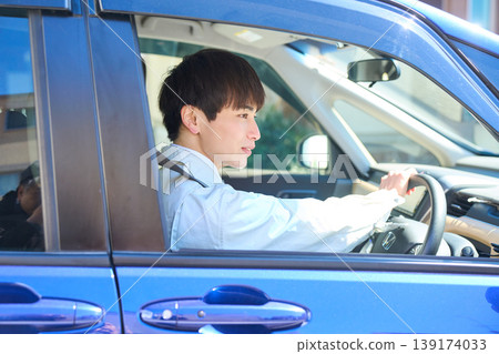 A young Japanese man in work clothes smiles and looks straight ahead from the driver's seat of a car. A young Japanese man in work clothes smiles and looks straight ahead from the driver's seat of a car. 139174033