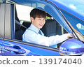 A young Japanese businessman smiles as he looks out the window from the driver's seat of his company car. 139174040