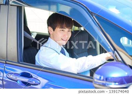 一位年輕的日本商人坐在公司車的駕駛座上,望著窗外,臉上帶著微笑。 一位年輕的日本商人坐在公司車的駕駛座上,望著窗外,臉上帶著微笑。 139174040
