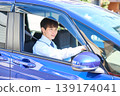 A young Japanese businessman smiles as he looks out the window from the driver's seat of his company car. 139174041