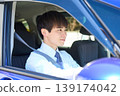 A young Japanese businessman smiles as he looks out the window from the driver's seat of his company car. 139174042