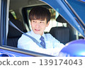 A young Japanese businessman smiles as he looks out the window from the driver's seat of his company car. 139174043