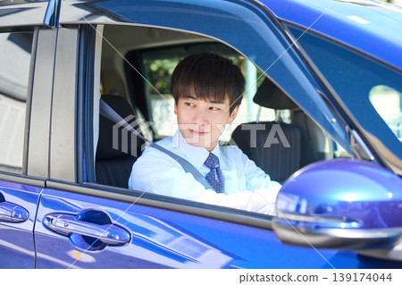 一位年輕的日本商人坐在公司車的駕駛座上,望著窗外,臉上帶著微笑。 一位年輕的日本商人坐在公司車的駕駛座上,望著窗外,臉上帶著微笑。 139174044