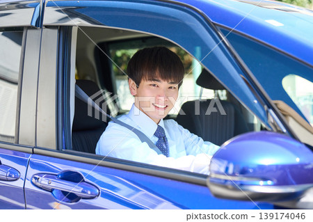 一位年輕的日本商人坐在公司車的駕駛座上,望著窗外,臉上帶著微笑。 一位年輕的日本商人坐在公司車的駕駛座上,望著窗外,臉上帶著微笑。 139174046