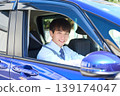 A young Japanese businessman smiles as he looks out the window from the driver's seat of his company car. 139174047