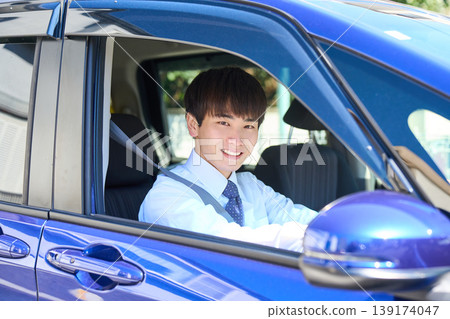 一位年輕的日本商人坐在公司車的駕駛座上,望著窗外,臉上帶著微笑。 一位年輕的日本商人坐在公司車的駕駛座上,望著窗外,臉上帶著微笑。 139174047