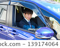 A young Japanese businessman looks at the camera through the window from the driver's seat of his company car. 139174064