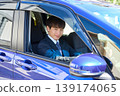 A young Japanese businessman looks at the camera through the window from the driver's seat of his company car. 139174065
