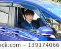 A young Japanese businessman looks at the camera through the window from the driver's seat of his company car. 139174066