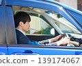 A Japanese businessman in a suit sits in the driver's seat of a car, facing forward and focusing on safe driving. 139174067