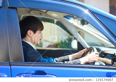 A Japanese businessman in a suit sits in the driver's seat of a car, facing forward and focusing on safe driving. A Japanese businessman in a suit sits in the driver's seat of a car, facing forward and focusing on safe driving. 139174067