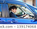 A Japanese businessman in a suit sits in the driver's seat of a car, facing forward and focusing on safe driving. 139174068