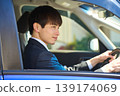 A Japanese businessman in a suit sits in the driver's seat of a car, facing forward and focusing on safe driving. 139174069