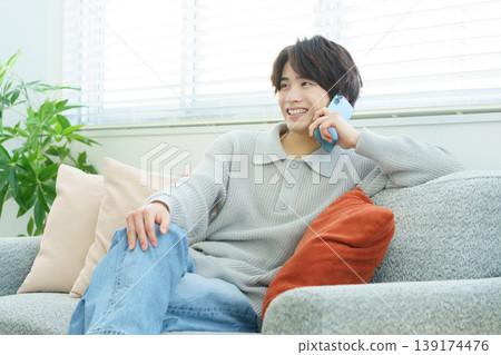 一位年輕的日本男子在客廳裡拿著他的智慧型手機。 139174476