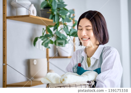 A smiling Asian woman surrounded by the fresh scent of laundry. A smiling Asian woman surrounded by the fresh scent of laundry. 139175338