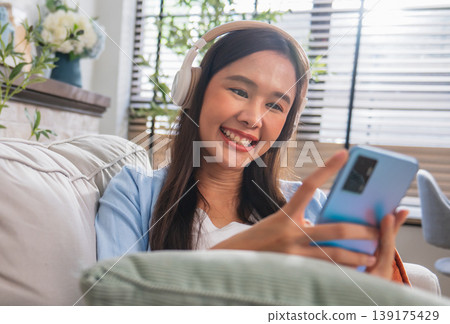Young woman smiles while using smartphone indoors Young woman smiles while using smartphone indoors 139175429