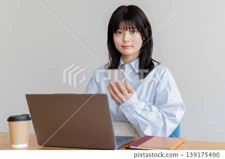 A woman using a computer while looking at her smartphone. A woman using a computer while looking at her smartphone. 139175490