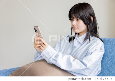 A woman sitting on a couch and operating a smartphone 139175507