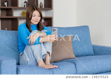 在沙發上使用智能手機的年輕女士 在沙發上使用智能手機的年輕女士 139175523