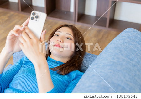 A woman lying on the sofa and looking at her smartphone 139175545
