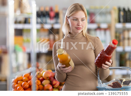 Young woman buyer chooses tomato and peach juices Young woman buyer chooses tomato and peach juices 139175555
