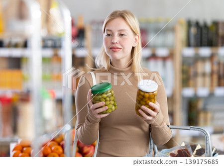 Girl buyer examine good, doubt and choose pickled olives in store 139175685