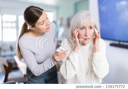 Elderly businesswoman suffers from a headache. Colleague offers her headache pills. Elderly businesswoman suffers from a headache. Colleague offers her headache pills. 139175772