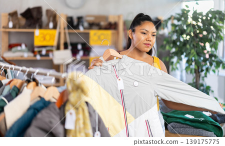 Woman chooses coat for the winter period in fashionable clothing store 139175775