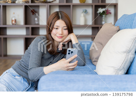 一位神態放鬆的女士正在看智慧型手機；一種在家裡的沙發上放鬆身心的生活方式。 139175798