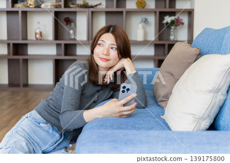 一位神態放鬆的女士正在看智慧型手機;一種在家裡的沙發上放鬆身心的生活方式。 一位神態放鬆的女士正在看智慧型手機;一種在家裡的沙發上放鬆身心的生活方式。 139175800