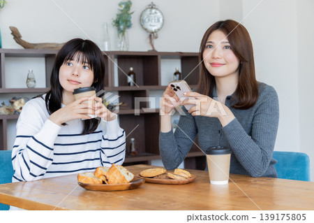 兩名女子在咖啡館放鬆,各自看著自己的智慧型手機。 兩名女子在咖啡館放鬆,各自看著自己的智慧型手機。 139175805