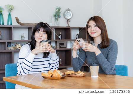 兩名女子在咖啡館放鬆，各自看著自己的智慧型手機。 139175806