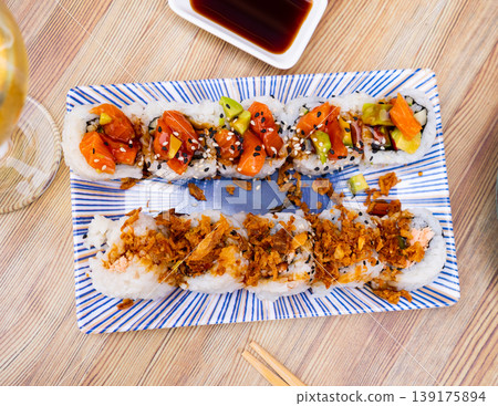 On table there is plate with set of sushi - uramaki rolls with cucumber, avocado crab and salmon On table there is plate with set of sushi - uramaki rolls with cucumber, avocado crab and salmon 139175894
