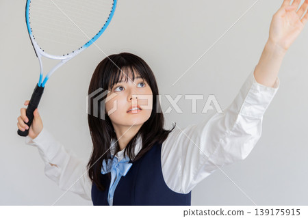 A high school girl performing a serve motion with a tennis racket. 139175915