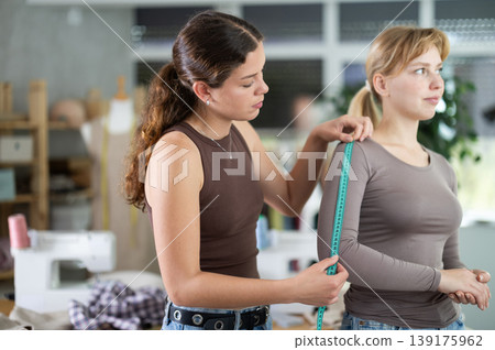 Female dressmaker taking measurements from client in sewing studi 139175962