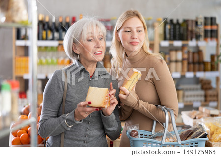 Girl and grandmother buyers examine good, doubt and choose cheese in store Girl and grandmother buyers examine good, doubt and choose cheese in store 139175963