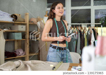 Smiling young female dressmaker posing in sewing studio 139175965