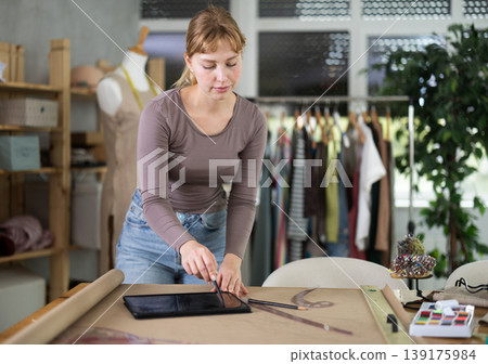 Young female dressmaker drawing in tablet in sewing workshop Young female dressmaker drawing in tablet in sewing workshop 139175984