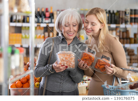 Girl and grandmother buyers examine good, doubt and choose prawn in store 139176075