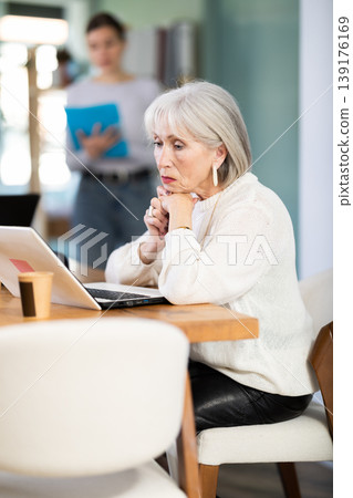 Elderly woman working on laptop adult colleague shows document Elderly woman working on laptop adult colleague shows document 139176169