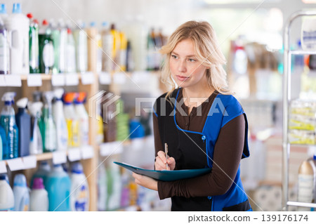 Woman seller, with papers and invoices in hands, makes inventory in store Woman seller, with papers and invoices in hands, makes inventory in store 139176174