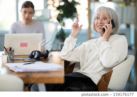 Adult woman judging female colleague talking on mobile phone Adult woman judging female colleague talking on mobile phone 139176177