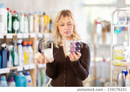 Girl housewife in household store examines goods, chooses candle Girl housewife in household store examines goods, chooses candle 139176201