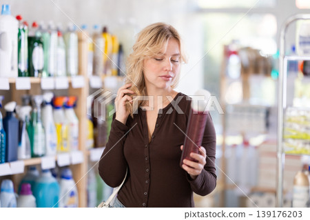 Happy young girl emotionally choosing aerosol hairspray in cosmetics store 139176203