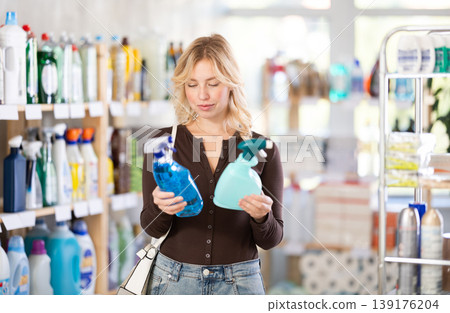 Girl housewife in household store examines goods, chooses glass cleaner spray Girl housewife in household store examines goods, chooses glass cleaner spray 139176204